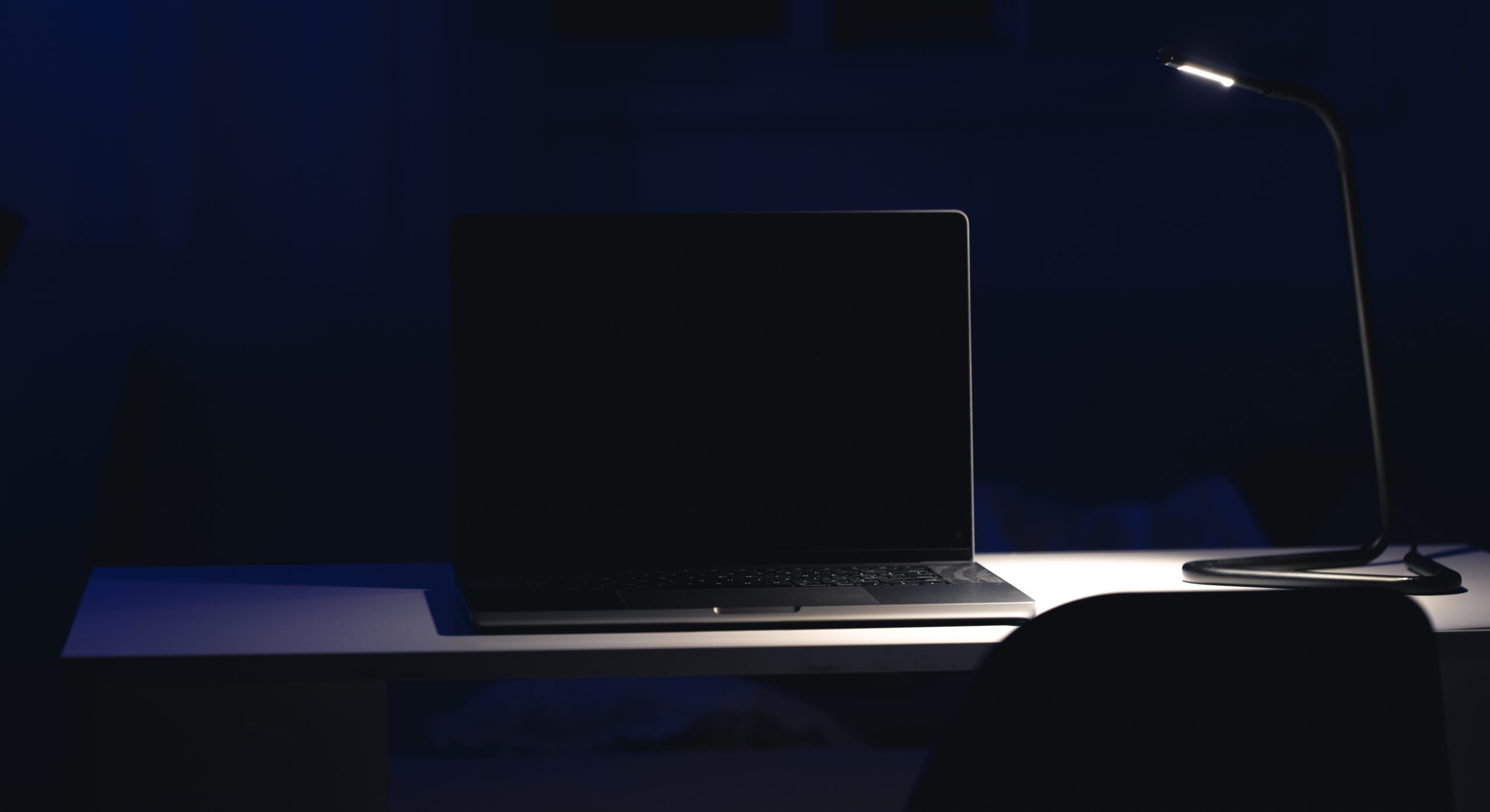 Donkere laptop op een bureau bij een bureaulamp, passend bij online bedreigingen en swatting in Nederland.