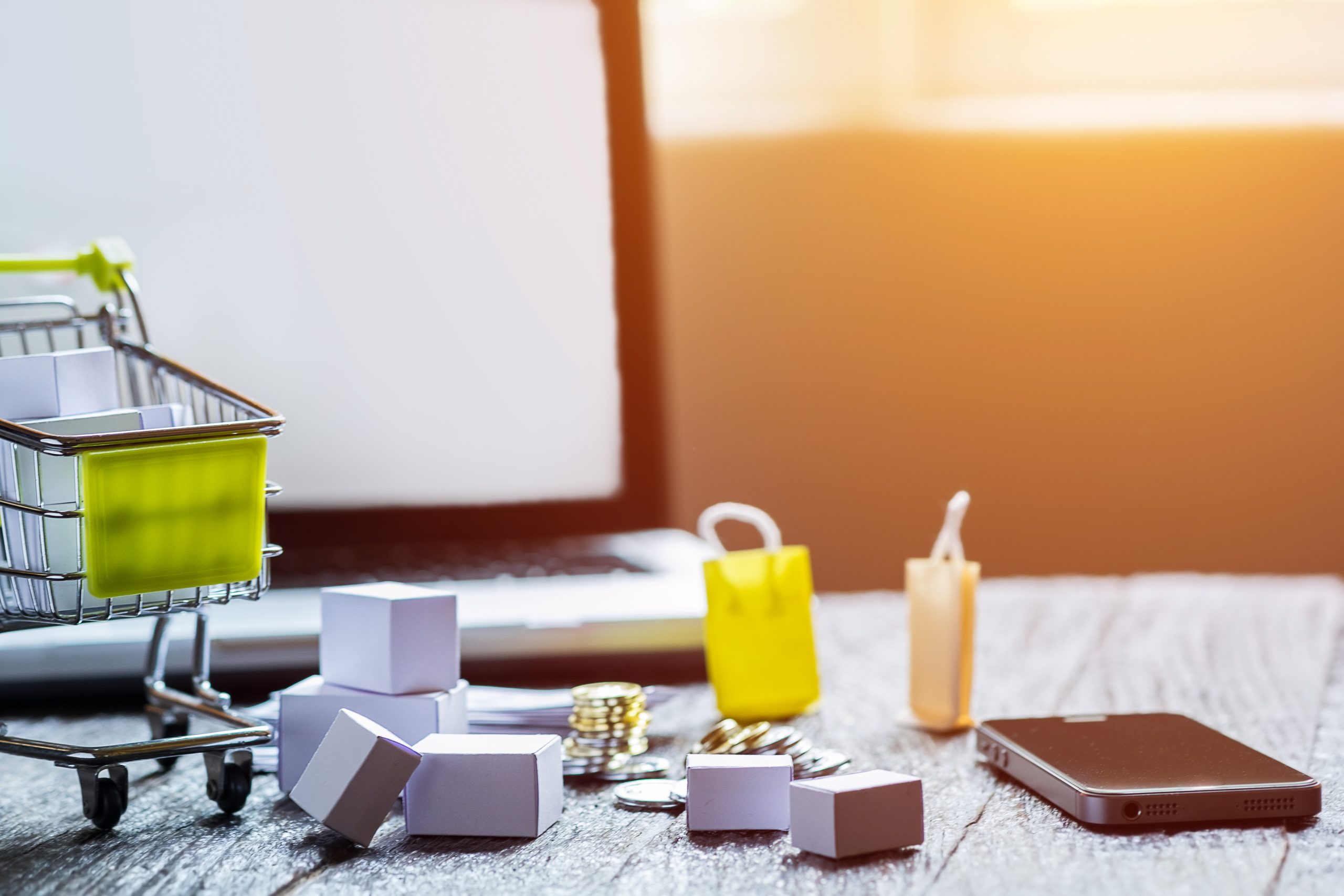 Winkelwagentje, smartphone, laptop en kleine pakketjes op een tafel als symbool voor online ondernemen en verkopen via digitale platforms.