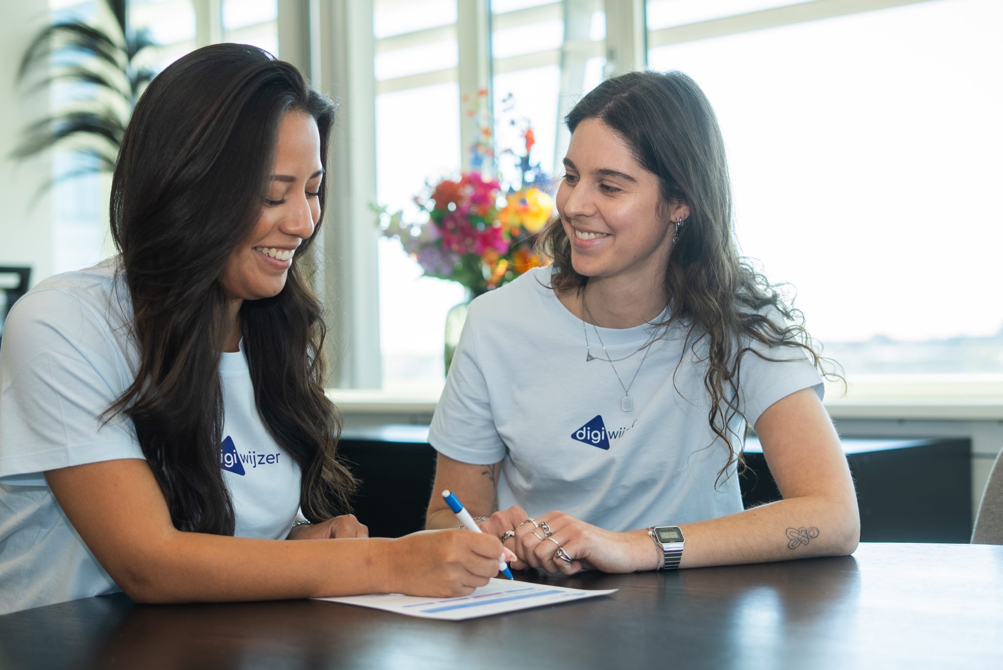 Twee medewerkers van Digiwijzer werken samen aan een praktische opdracht op papier.