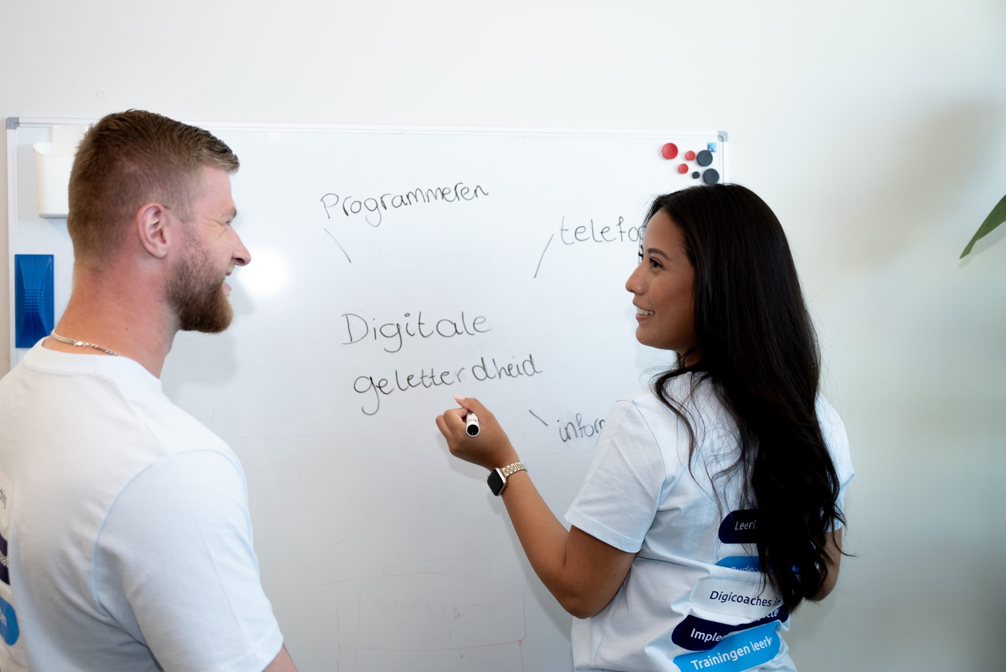 Twee medewerkers van Digiwijzer bespreken digitale geletterdheid bij een whiteboard met de verschillende onderdelen van het vakgebied.