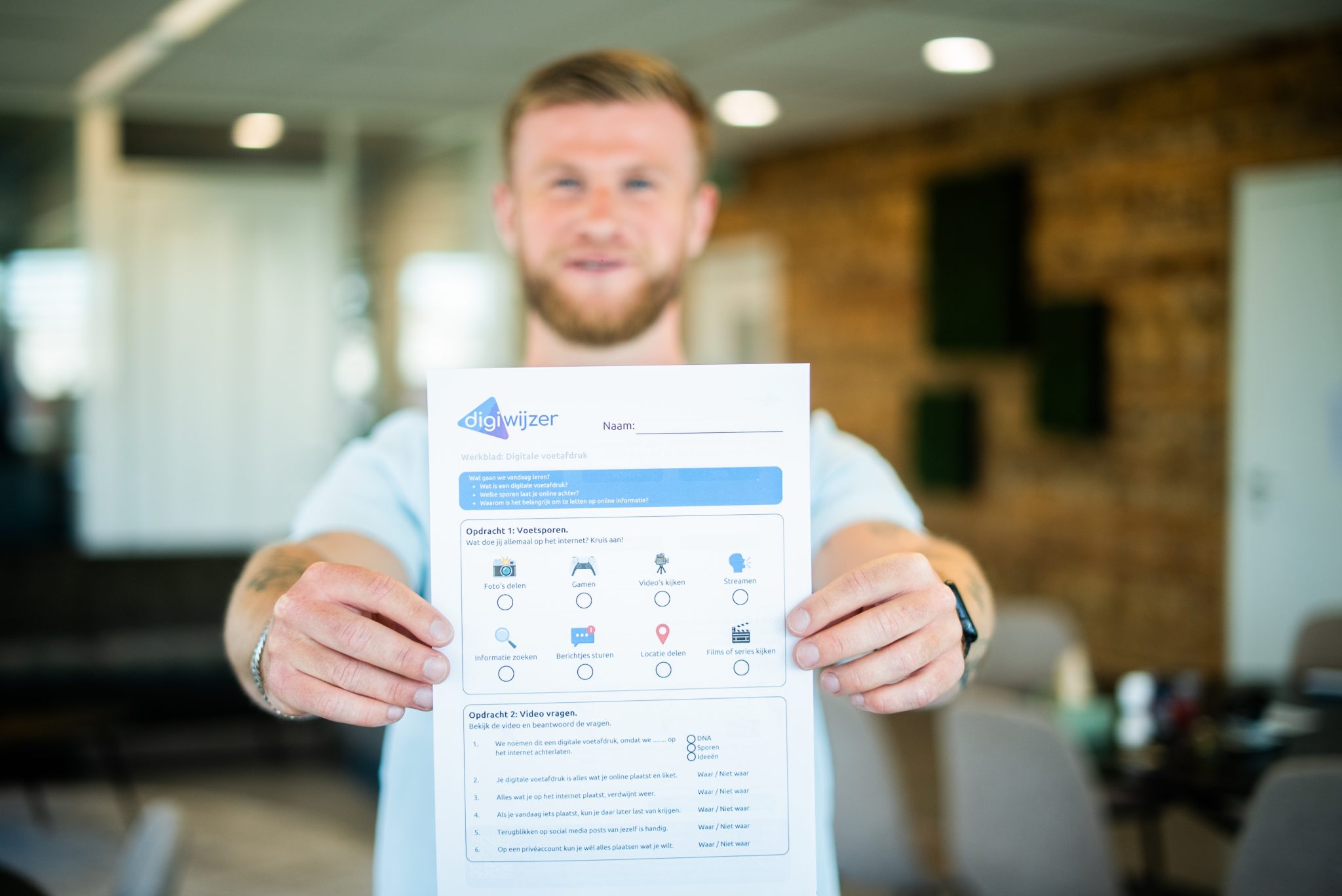 Medewerker van Digiwijzer houdt een werkblad over de digitale voetafdruk vast tijdens een les praktische ICT-vaardigheden.
