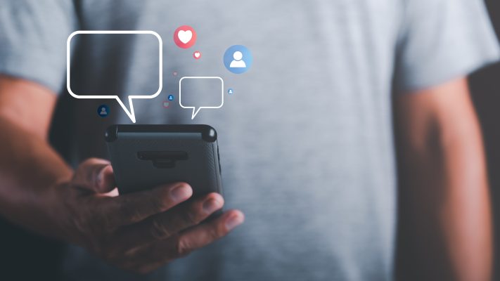 Persoon houdt een smartphone vast terwijl digitale chatballonnen en pictogrammen van sociale media boven het scherm zweven. De afbeelding symboliseert de verschuiving van WhatsApp naar andere chatplatformen zoals Snapchat, Discord, Instagram DM en TikTok DM.