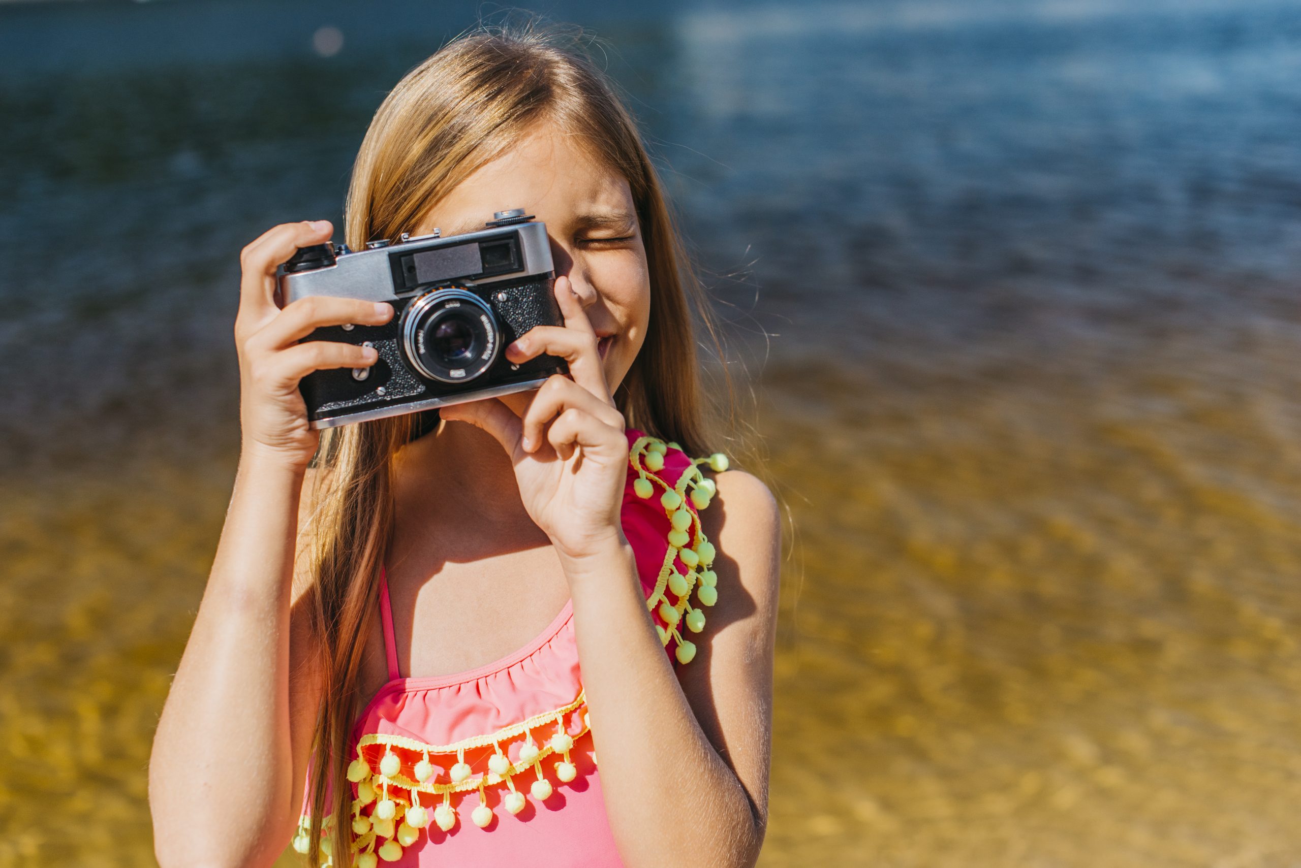 Kind maakt een foto met een camera aan het water, als illustratie bij een blog over het online delen van foto's van kinderen en AI.