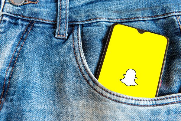 Smartphone met Snapchat-logo in een spijkerbroekzak, passend bij Snapchat advertenties in chats.